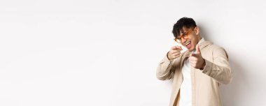 Gözlüklü yakışıklı, gülümseyen, kamerayı işaret eden, seni seçen ya da davet eden, beyaz arka planda duran komik adam..