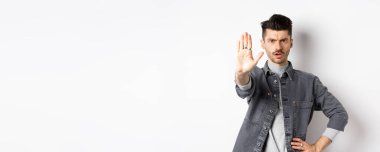 Ciddi bir adam durmasını, bir şeyi yasaklamasını ve kaşlarını çatmasını söyler, hayır der, elini beyaz arka plana uzatmaktan rahatsız olur..