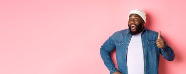 Mutlu Afro-Amerikan erkek manken başparmağını kaldırıyor ve evet diyor memnun, pembe arka planda duruyor..