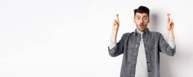 Heyecanlı genç adam şans dilemek ve nefes nefese kalmak için dua ediyor. Önemli haberleri bekliyor, yalvarıyor ya da dua ediyor, beyaz arka planda duruyor..