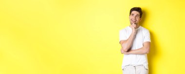 Gülümseyen bir adamın portresi sol üst köşede düşünceli görünüyor, bir şey seçiyor, bir fikri var, sarı arka planda duruyor..