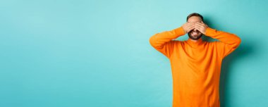 Mutlu sakallı adam sürpriz bekliyor, kulaklarını kapatıp hediyeler veriyor, açık mavi arka planda duruyor..