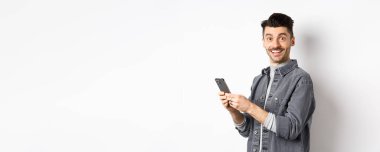 Akıllı telefon kullanıp kameraya bakan yakışıklı bir genç. Beyaz arka planda duran, gülen yüzlü, telefonda konuşan beyaz bir adam..