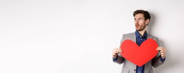 Adam, elinde büyük kırmızı kalp kesiği olan, beyaz arka planda Sevgililer Günü 'nde duran güzel birine hayret ediyor. Boşluğu kopyala