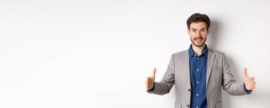 Heyecanlı yakışıklı iş adamı uzun boyda bir şey gösteriyor. Ellerini uzatıp beyaz arka planda duran büyük bir nesne..