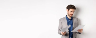 Takım elbiseli bir işadamı gazetelere bakıyor, işte belgeler okuyor, beyaz arka planda meşgul duruyor..