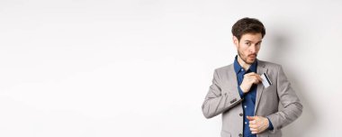 İş adamı kredi kartını takım elbisenin cebine koyar ve ıslık çalar, alışveriş yapar, beyaz arka planda durur..