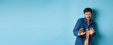 Adam siner ve çirkin şeylerden uzak durur, yana bakar ve kötü anlaşmayı reddetmek için ellerini uzatır, mavi arka planda durur..