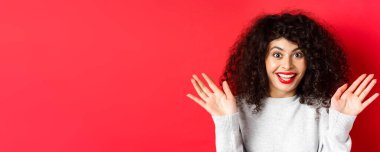 Şaşırmış ve mutlu kadının yakın çekimi harika haberler duyuyor, muhteşem bir olaya tepki veriyor, ellerini kaldırıyor ve sevinçten çığlık atıyor, eğleniyor, kırmızı arka planda duruyor..