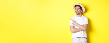 Turizm ve yaşam tarzı kavramı. Mutlu turist tanıtımı yapıyor, memnun görünüyor ve sol üst köşedeki logoyu işaret ediyor, sarı arka plan..