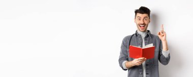 Heyecanlı adam ödevini yaparken bir fikir sunuyor, parmağını kaldırıyor ve planlayıcıyı tutuyor, beyaz arka plana karşı duruyor..