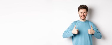 Gülümseyen yakışıklı adam iyi bir seçim yapıyor ve onaylıyor. Övüyor ya da tavsiye ediyor. Beyaz arka planda duruyor..