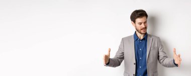Heyecanlı yakışıklı iş adamı uzun boyda bir şey gösteriyor. Ellerini uzatıp beyaz arka planda duran büyük bir nesne..