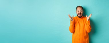 Heyecanlı ve mutlu sakallı bir adamın görüntüsü, el sıkışıyor ve şaşkın bir şekilde gülümsüyor, büyük haberler veriyor, açık mavi arka planda duruyor..