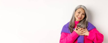 Tarz sahibi Asyalı annenin kalbi ile el ele tutuşması, dokunmuş ve yürekten bakması, teşekkür etmesi, beyaz arka planda durması..