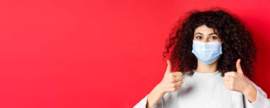 Sağlıklı insanlar ve covid-19 konsepti. Kıvırcık saçlı, salgın sırasında kendini korumak için tıbbi maske takan gülümseyen kadının yakın plan portresi..