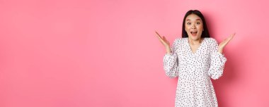 Mutlu ve şaşırmış Asyalı kadın seviniyor, ellerini açıyor ve hayretle nefes nefese, heyecan ve inançsızlıkla bakıyor, pembe arka planda duruyor..