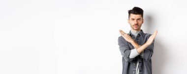 Kızgın adam durmak ya da hayır demek için çapraz hareket gösterir, kaşlarını çatar ve ciddidir, aynı fikirde değildir ve kötü durumu engeller, beyaz arka planda durur..