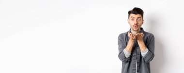 Romantik yakışıklı bir adam havada öpüşüyor, kameraya bakıyor, beyaz arka planda modaya uygun kıyafetler giyiyor..