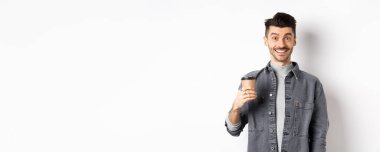 Hevesli yakışıklı bir adam kahve fincanı tutuyor ve gülümsüyor, kafeteryadan güzel bir içki içiyor, beyaz arka planda duruyor..