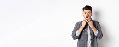 Şok olmuş, beyaz adam soluk soluğa kalmış, ağızını ellerle kapatmış ve korkunç bir şeye bakıyor, kötü bir kazaya tanık oluyor, aman Tanrım, beyaz arka planda duruyor..