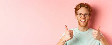 Memnun erkek müşterinin yüzü onaylanmış, mutlu gülümsüyor, gözlük ve tişört takıyor, pembe arka plan.