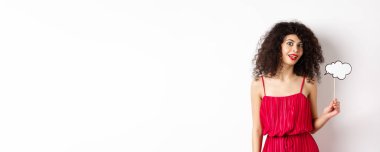 Kıvırcık saçlı, kırmızı elbiseli, yorum bulutu tutan, beyaz arka planda duran güzel bir kadın..