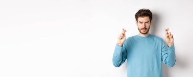 Umut dolu ve kendinden emin genç adam şans dilemek ya da dua etmek için parmaklarını çapraz yapıyor, sonuçları tahmin ediyor, beyaz arka planda duruyor..