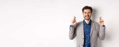 Umut dolu gülümseyen işadamı iyimser görünüyor, şans diliyor, kazanmak için dua ediyor, umutla sonuçları bekliyor, beyaz arka planda duruyor..