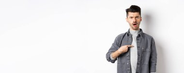 Genç bir adamın suçlanması, kaşlarını çatması ve kendini göstermesi, şok olması, beyaz arka planda durması rahatsız edici..