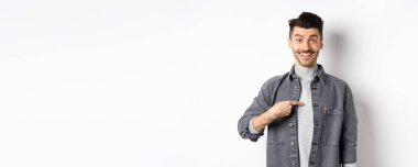 Sorun bende mi? Şaşırmış mutlu adam kendini işaret ediyor, gülümsüyor, seçiliyor, bahar kıyafetiyle beyaz arka planda duruyor..