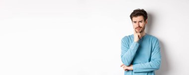 Şüpheci genç adam somurtuyor, endişeli düşünceli bakıyor, beyaz arka plan üzerinde üzgün duruyor.