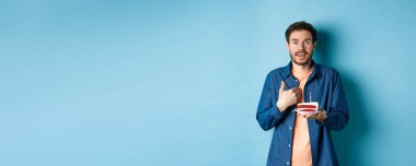 Kutlama ve tatil konsepti. Elinde mumla doğum günü pastası tutan ve kendini inançsızlıkla işaret eden şaşırmış adam, doğum günü kutlaması, mavi arka plan.