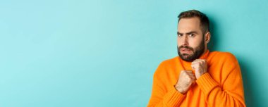 Korkmuş ve hoşnutsuz görünen, korkudan atlayan, açık mavi arka planda duran, korkmuş sakallı adamın yakın çekimi..