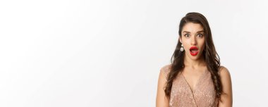 Kırmızı dudaklı, saç stili, elbise giyen, kameraya şaşırmış beyaz arka planda duran çekici bir kadın..