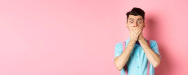 Şok olmuş ve nutku tutulmuş adam ağzını kapattı, elleriyle dudaklarını kapadı ve kameraya baktı, pembe arka planda duruyordu..