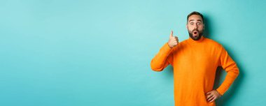 İyi iş çıkardın. Yakışıklı sakallı adam baş parmağını gösterip, iyi işi övüyor, mükemmel bir ürün öneriyor, onaylıyor ve onaylıyor, gülümsüyor, açık mavi arka planda duruyor..
