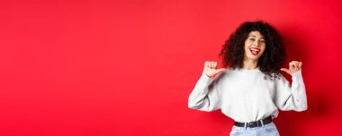 Kırmızı dudaklı, kendine güvenen, kendini beğenmiş, gösteriş meraklısı, kırmızı arka planda duran kendine güvenen genç bir kadın..