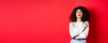 Gülümseyen mutlu bir kadının yüzü yana dönük, kararlı bir şekilde yukarı bakıyor, bir şey seçiyor, kırmızı arka planda verdiği karardan emin duruyor..