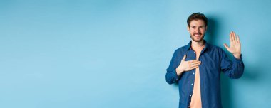 Dürüst genç adam gülümsüyor ve söz veriyor, el ele tutuşuyor, yemin ediyor ya da yemin ediyor, doğruyu söyleyeceğine, mavi arka planda duracağına yemin ediyor..