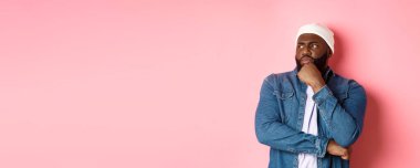 Düşünceli Afro-Amerikan erkek model karar veriyor, endişeli görünüyor, düşünüyor ya da şüphe duyuyor, pembe arka planda duruyor..