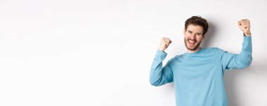 Mutlu genç adamın zafer kazanması, şampiyon gibi hissetmesi, tezahürat içinde kazanması ve çığlık atması, beyaz arka planda durması..