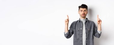 Üzgün, kaşları çatık adam yukarı bakıyor, beyaz arka planda tereddütlü duruyor..