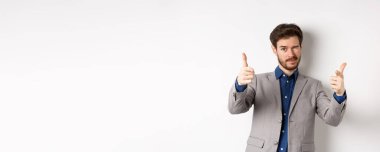 Sen halledersin. Beyaz takım elbiseli yakışıklı beyaz iş adamı kamerayı işaret ediyor ve göz kırpıyor, insanları motive ediyor, şirkette çalışmaya davet ediyor, beyaz arka planda duruyor..