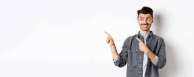 Mutlu yakışıklı adam gülümsüyor ve solu işaret ediyor, havalı ürünler gösteriyor, beyaz arka planda duruyor..