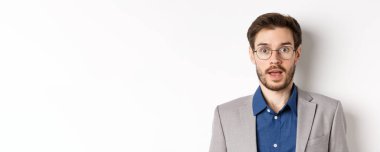 Gözlüklü ve takım elbiseli şaşkın iş adamının yakın çekimi hayret içinde, iyi haberleri duy, beyaz arka planda dur..