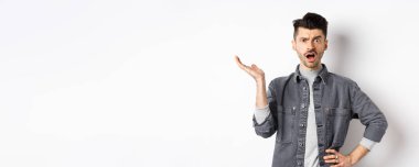 Kafası karışık ve sinirli adam elini kaldırıp şikayet ediyor, ne olduğunu soruyor, anlayamıyorum, beyaz arka planda duruyor..