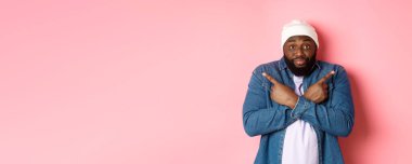Kafası karışmış siyahi bir adam seçiminde yardım ister, yan tarafı gösterir, kameraya bakar, karar verir, pembe arka planda durur..