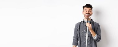 Yakışıklı, pozitif bir adam büyüteçle beyaz, mükemmel bir gülümseme ve şaşı bakışlar sergiliyor, komik suratlar yapıyor, beyaz arka plan..