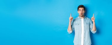 Mavi arka planda logo gösteren, parmaklarını havaya kaldıran yakışıklı bir adamın portresi..